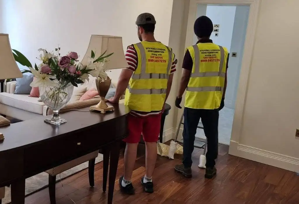 Two removal service provider man are standing beside a table for packing their client luggage and they are standing in his house