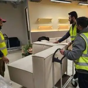 Movers in high-visibility vests transporting a sofa on a trolley during an indoor relocation.