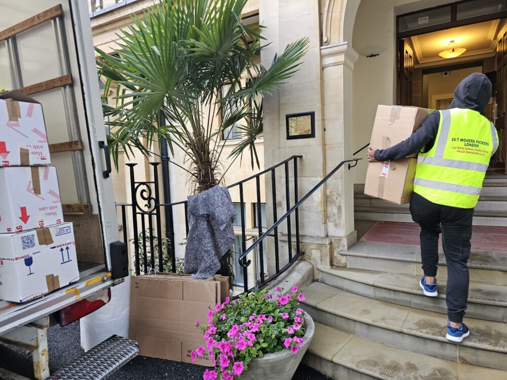 Removal company worker unloading boxes from a moving truck parked outside a residential building.