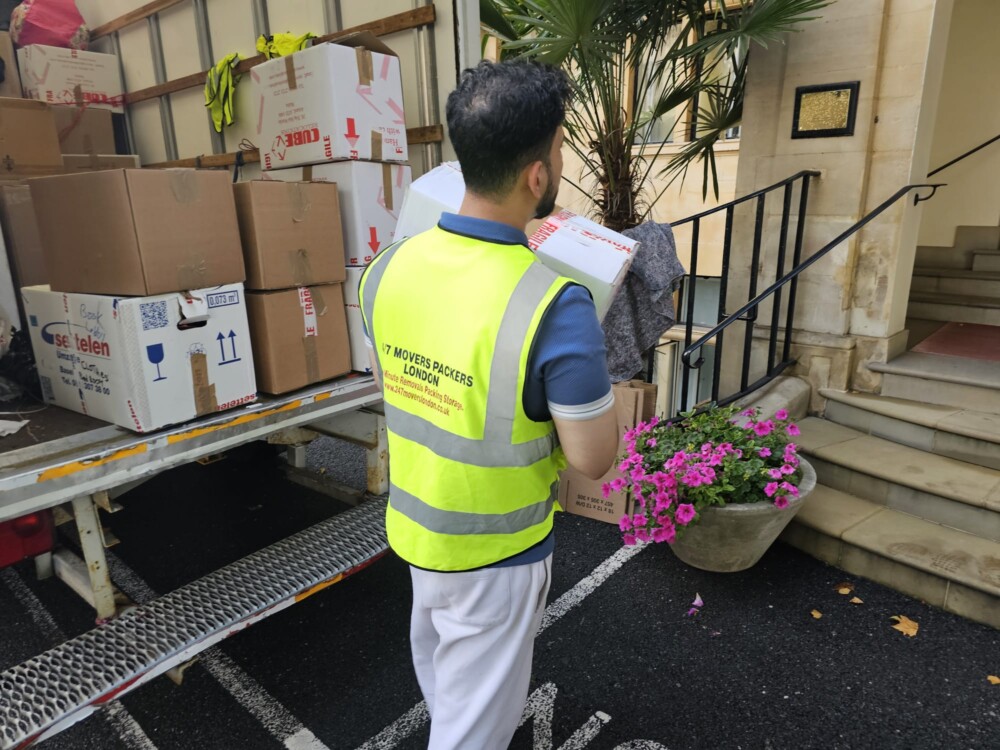 Removal company worker unloading boxes from a moving truck parked outside a residential building.