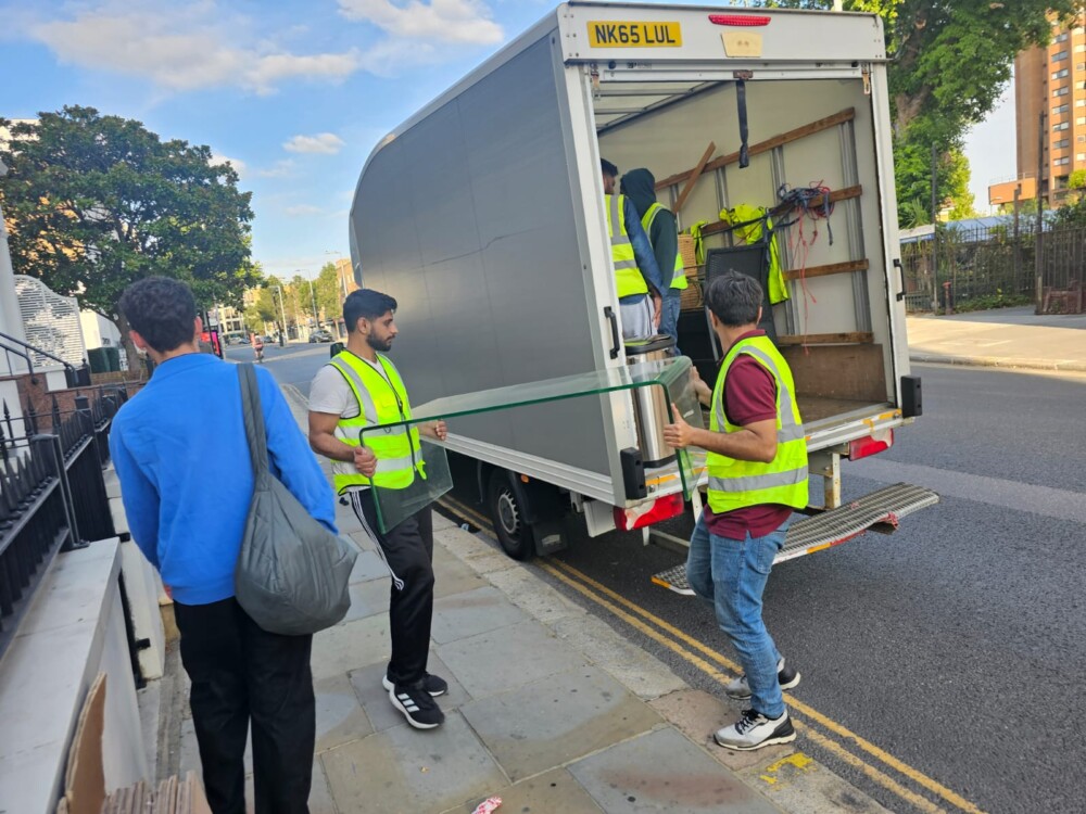 Movers in high-visibility vests unloading boxes and furniture from a truck on a London street.