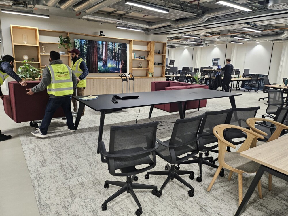 Team of professional movers relocating furniture and office equipment inside a modern workspace.