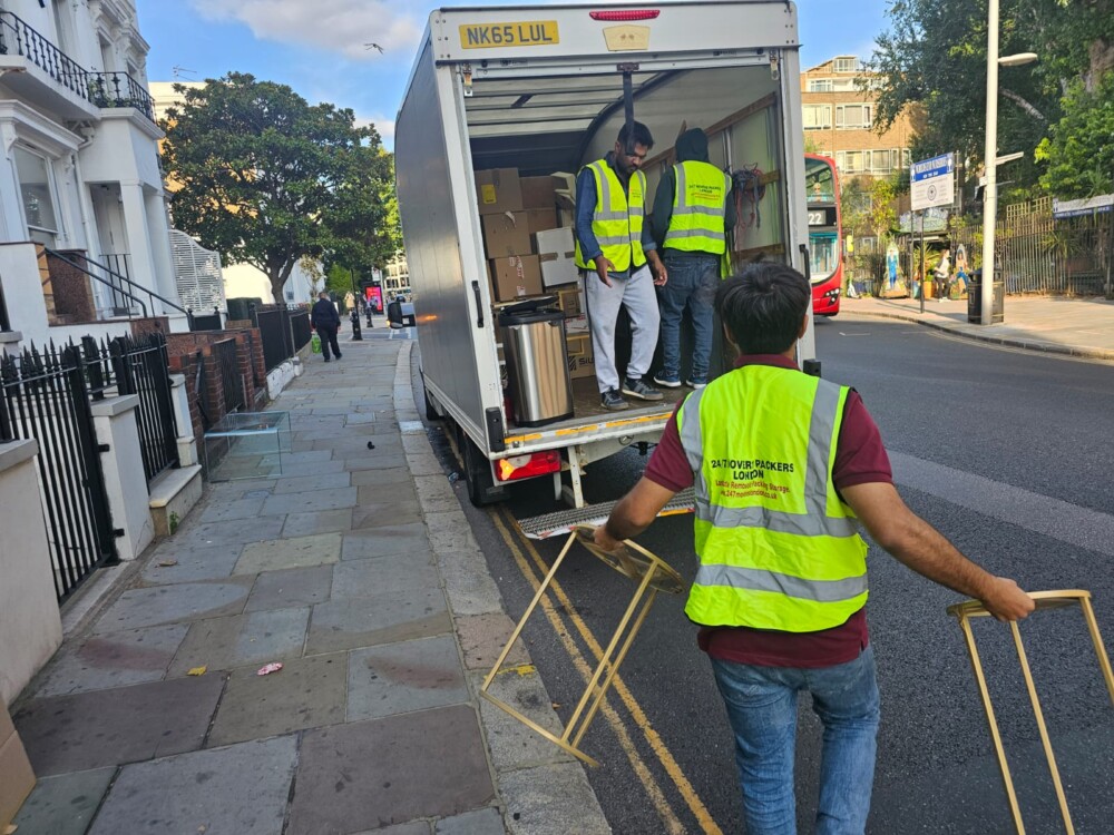 Movers in high-visibility vests unloading boxes and furniture from a truck on a London street.