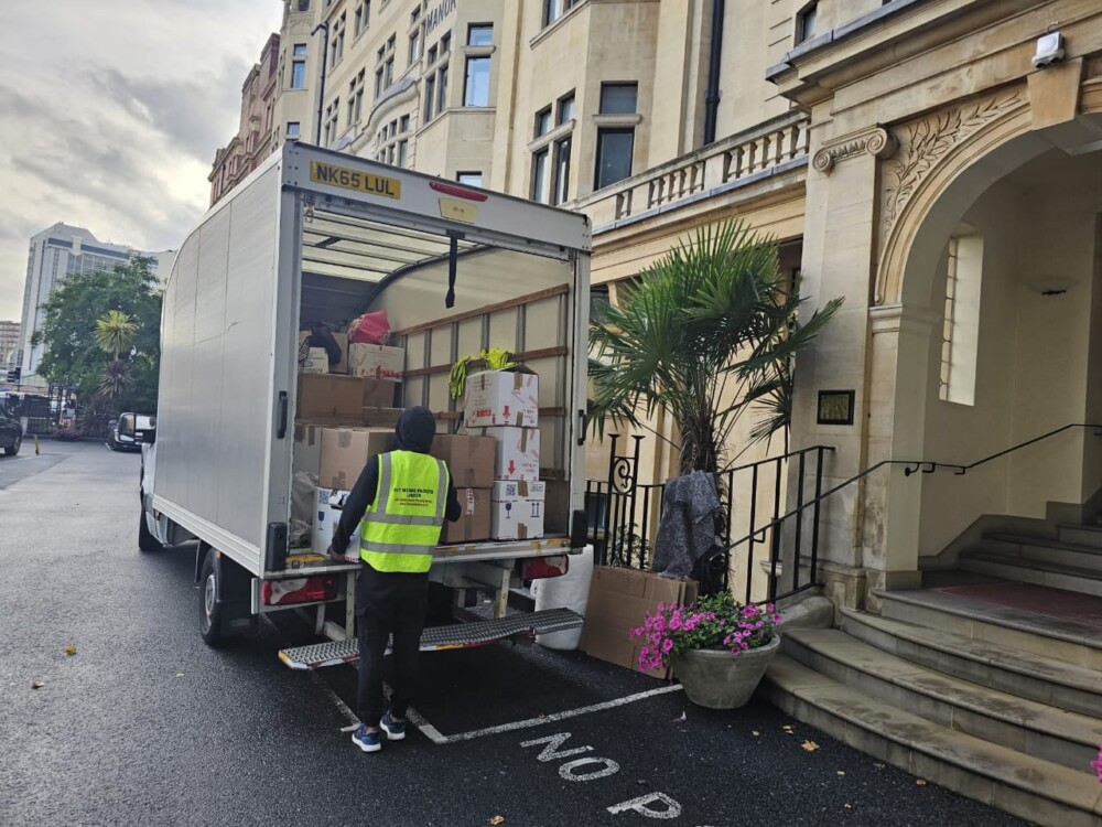 Removal company worker unloading boxes from a moving truck parked outside a residential building.